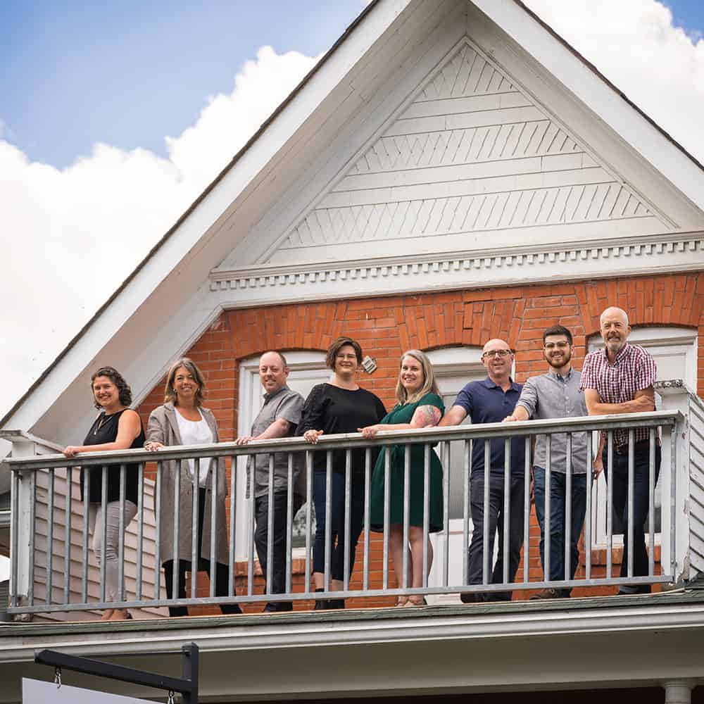 A team of residential designers in Calgary stand outside on the balcony of their office.